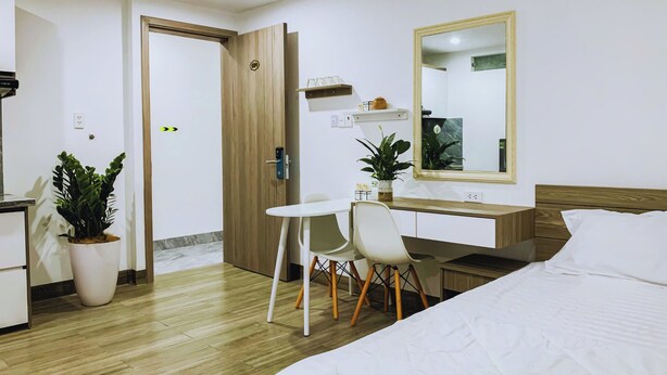 Ett hotellrum med en säng, ett skrivbord, en stol, en spegel och en krukväxt.