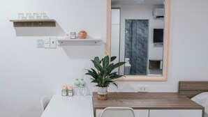 Ett modernt hotellrum med ett vitt bord, en träskommod, en spegel och en krukväxt.