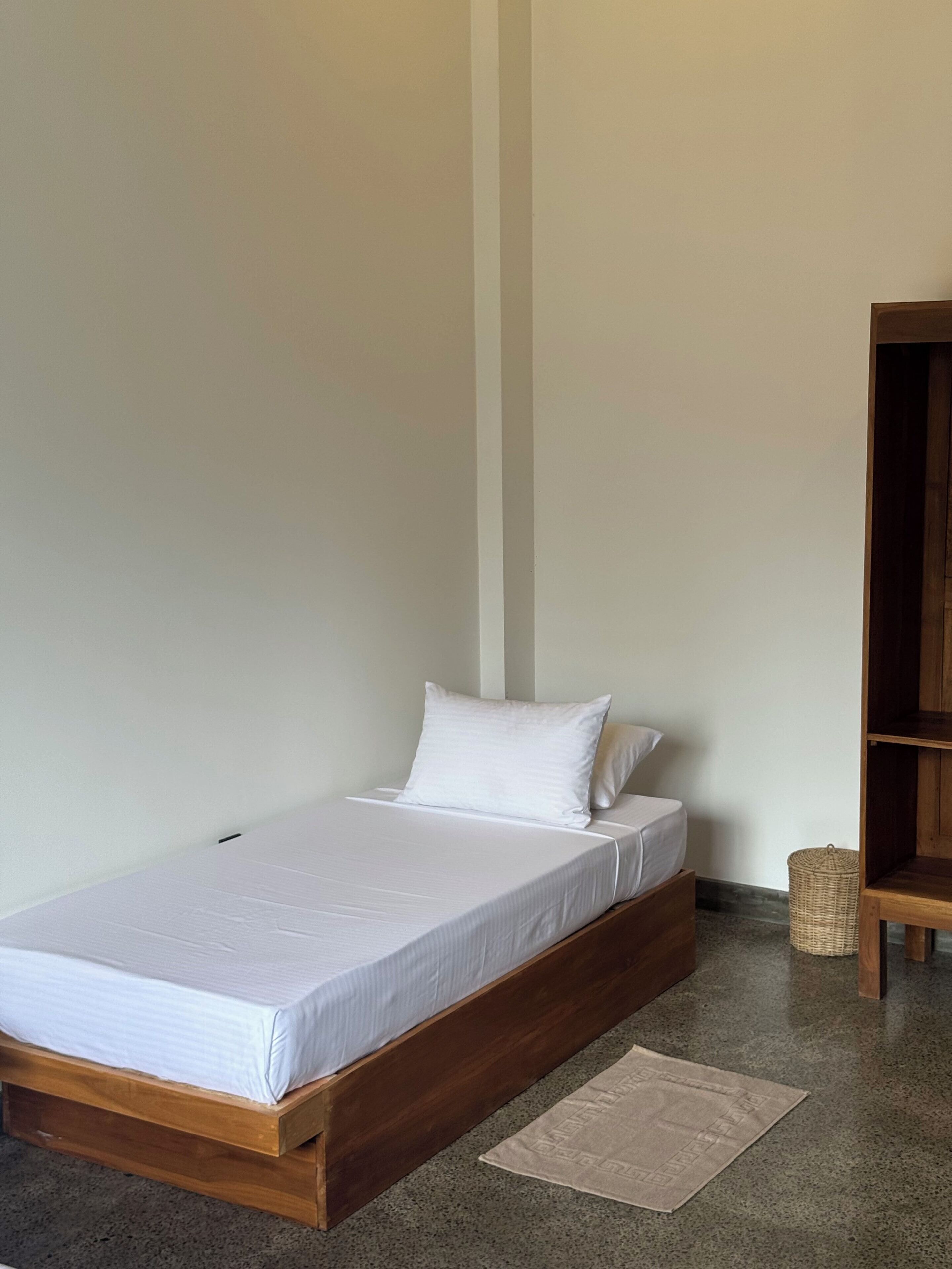 A single bed with white bedding in a room with a wooden headboard and a small woven basket beside it.