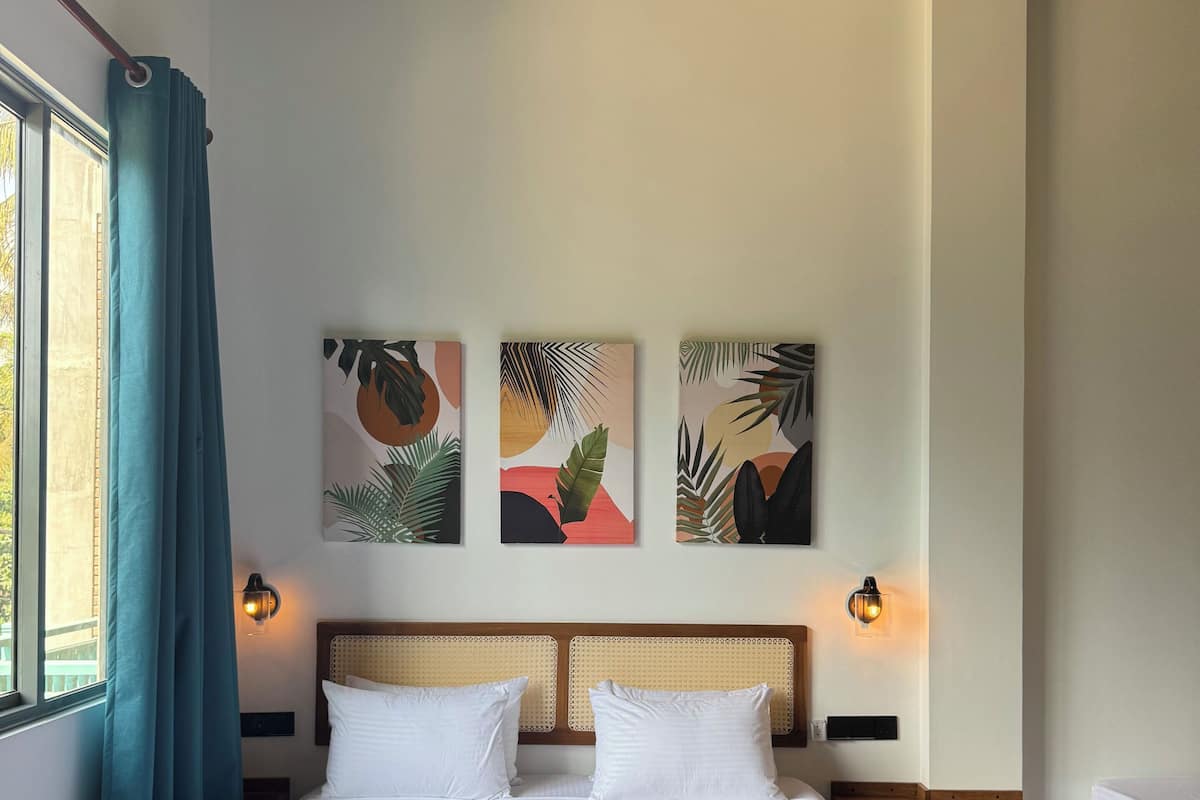 A hotel room with a large bed, two bedside tables, a ceiling fan, and wall-mounted artwork.