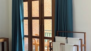Una habitación con puerta de madera con paneles de vidrio, cortinas color turquesa, un banco de madera y un perchero con toallas.