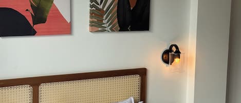 A hotel room with a bed, white pillows, a headboard, a wall-mounted light, and two pieces of wall art.
