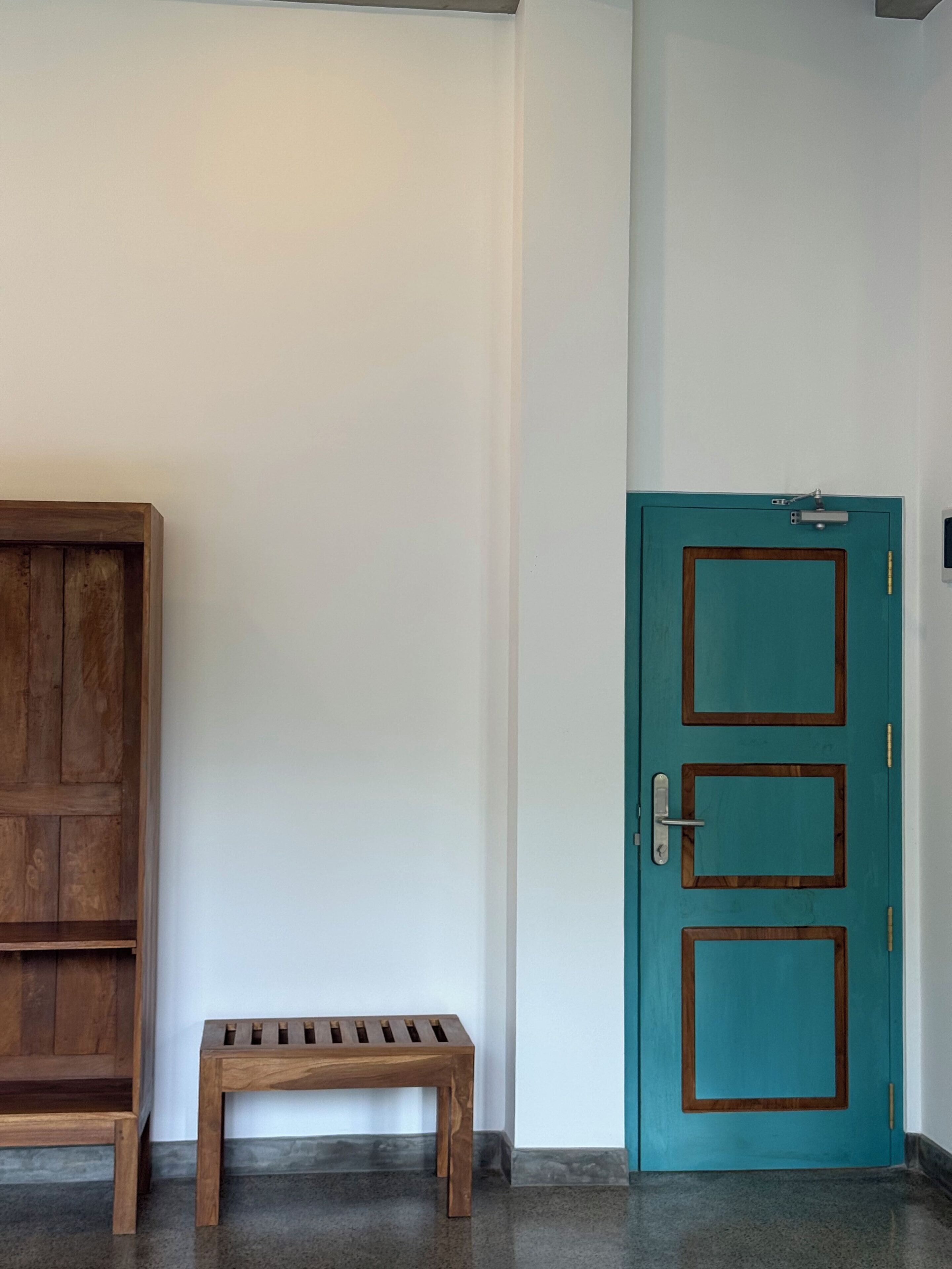 A hallway with a wooden bench, a teal door with a handle, and a white wall.