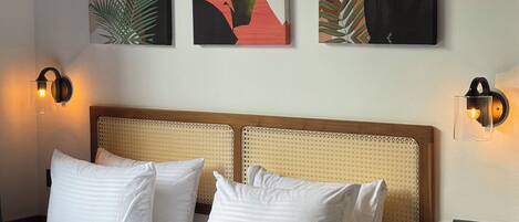 Una cama bien tendida con sábanas y almohadas blancas, un cabecero tejido y dos lámparas fijadas a la pared.