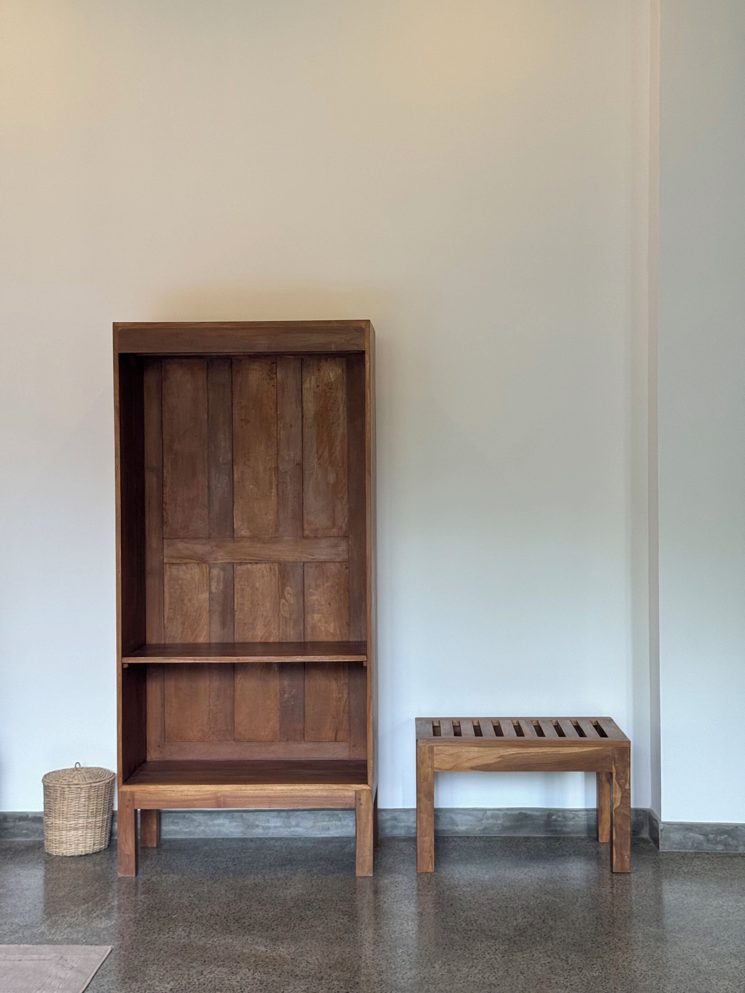A wooden cabinet with multiple shelves and a matching bench against a plain wall.