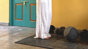 Una persona realizando un ejercicio con mancuernas en una habitación con una puerta azul verdosa y una pared amarilla.