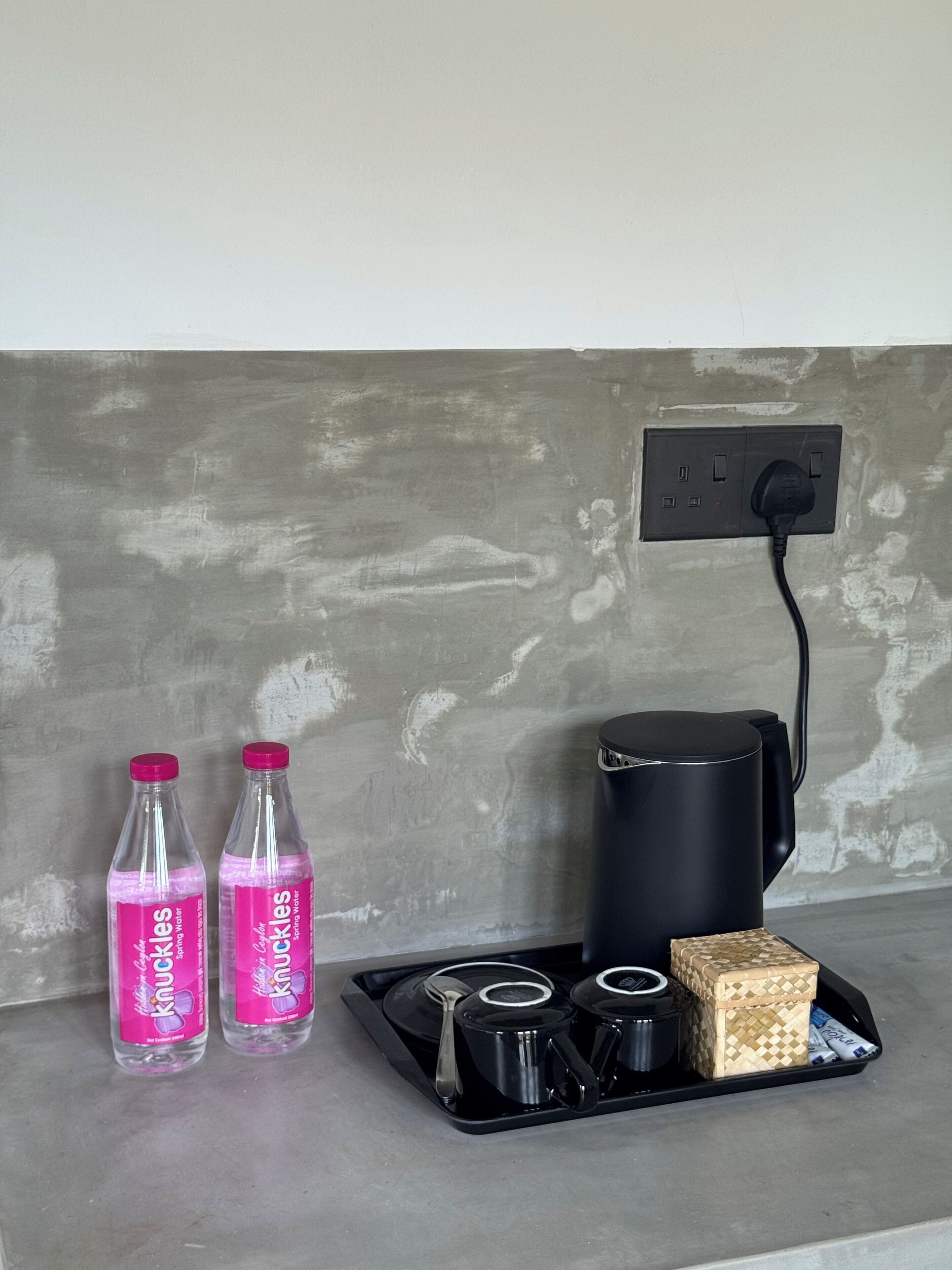 A countertop with two bottles of sparkling water, a black coffee maker, a tray with cups and a box, and a power outlet.