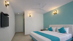 A hotel room with a bed, a flat-screen TV, a ceiling fan, and wall-mounted lights. - Rooms By DeVerveil (Mysore)