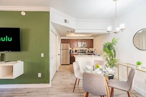 A modern living room with a flat-screen TV, a dining area with a glass table, and a kitchen in the background. - ASU Area Getaway with Pool, Spa, Gym & Parking (Tempe)