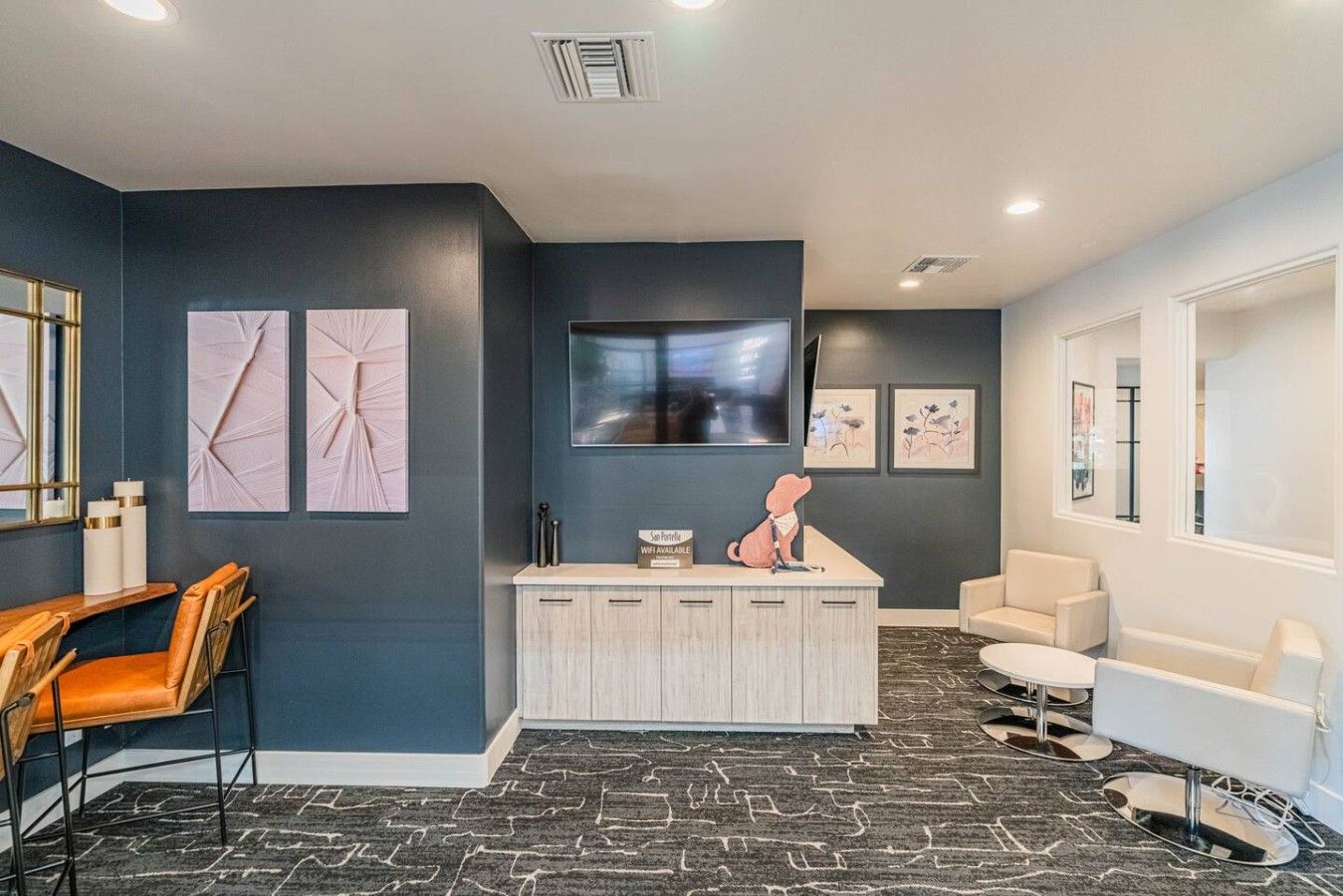 A modern reception area with a desk, chairs, artwork, and a large flat-screen TV.