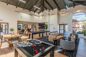 Un espacio interior moderno con mesa de billar, zonas de estar y una cocina al fondo.