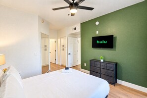 Ein Schlafzimmer mit einem Bett, einem Deckenventilator, einem an der Wand befestigten Fernseher und einer Kommode.