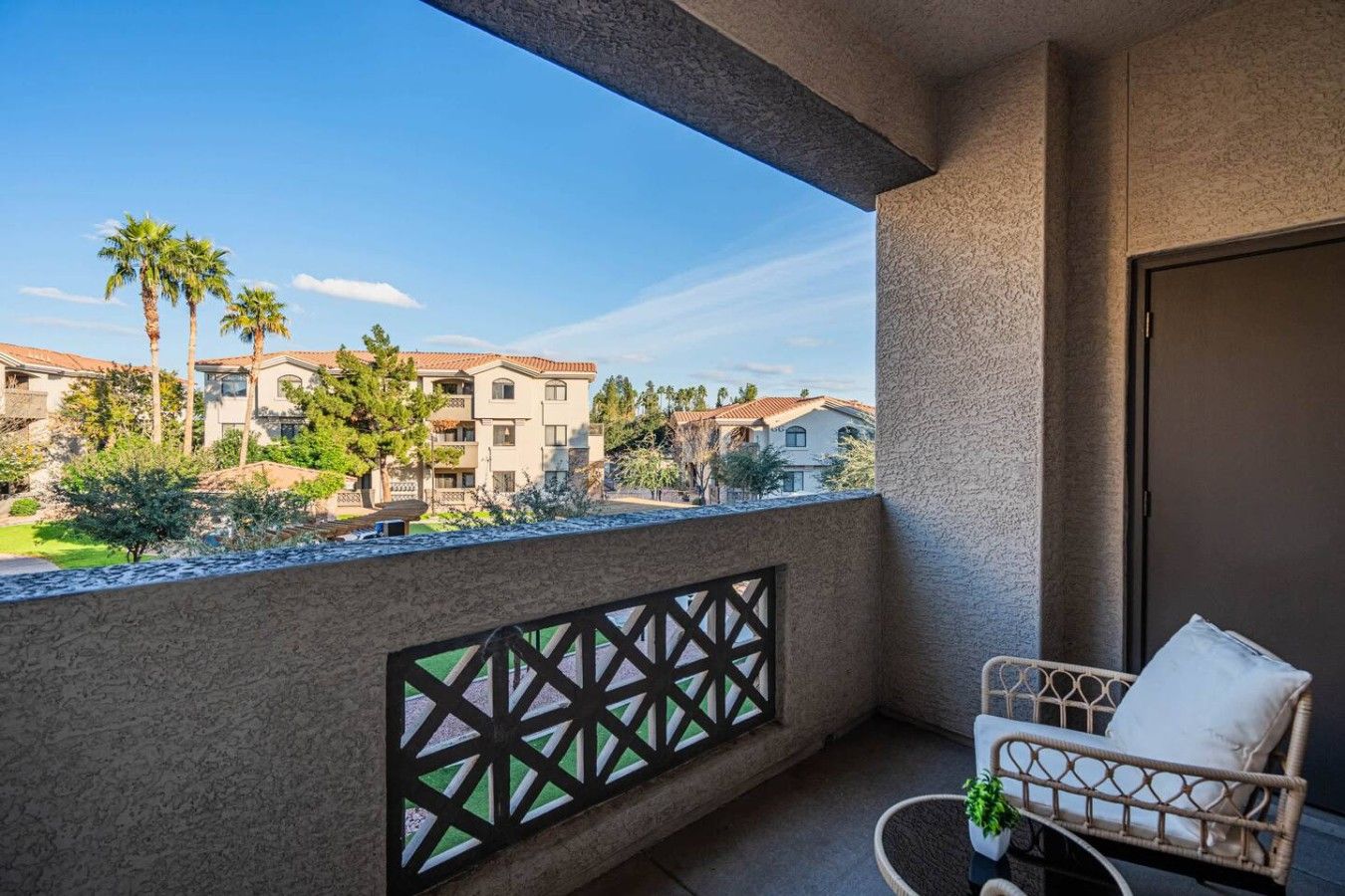 A balcony with a view of a residential area, a wicker chair, and a door.