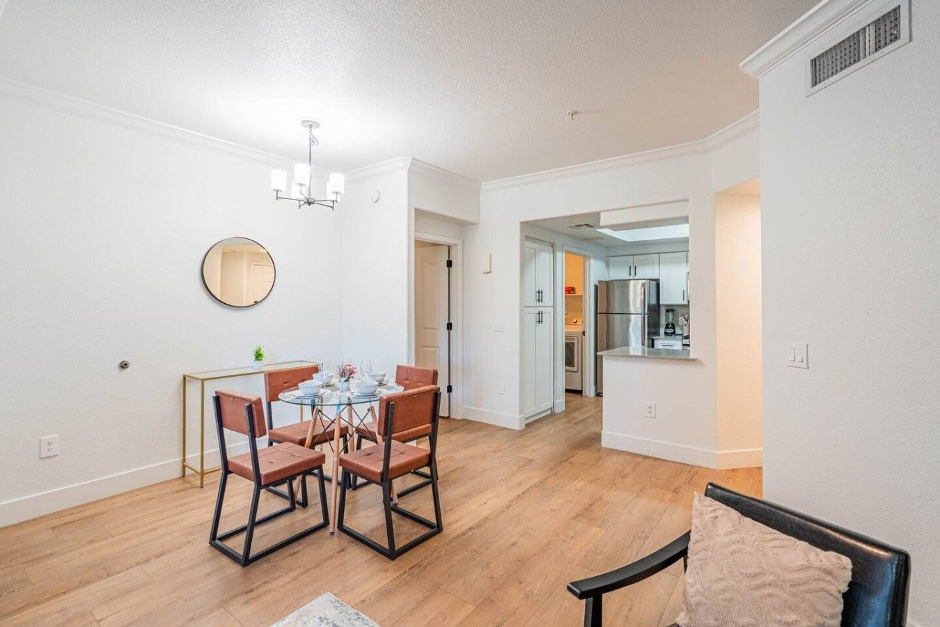 A modern kitchen with stainless steel appliances, a dining area with a round table and chairs, and a hallway leading to a bathroom.