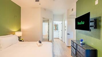 A hotel room with a bed, a TV mounted on the wall, and a dresser.