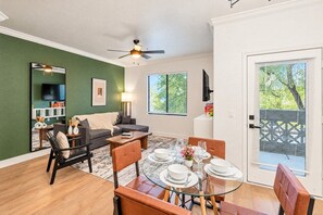 A dining area with a round glass table set for four, a sofa, and a television mounted on the wall. - Near Diablo Stadium & ASU-HotTub,Pool,Gym,Parking (Tempe)