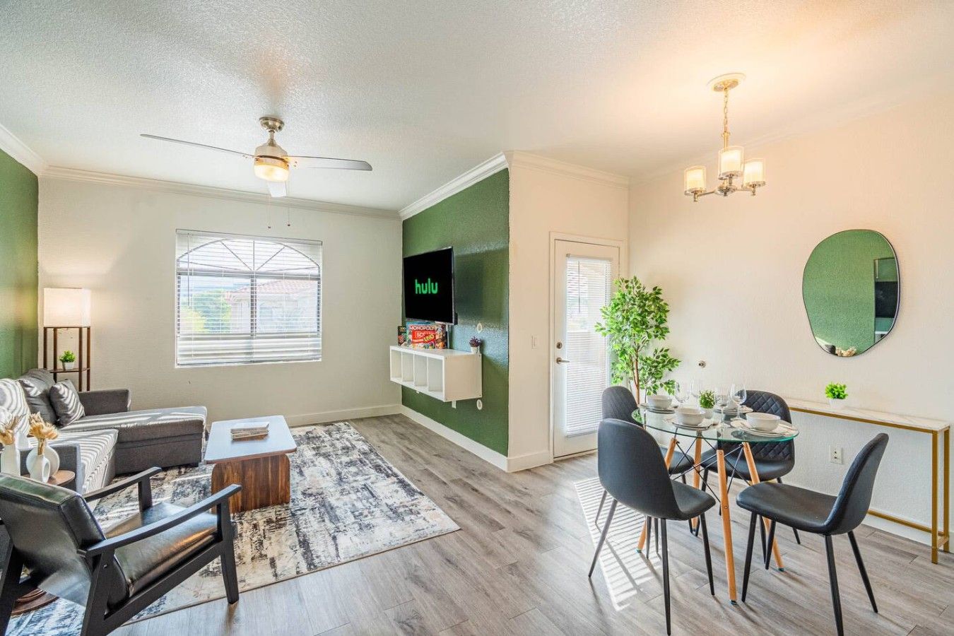 A modern living room with a sofa, coffee table, and TV. There is a dining area with chairs and a table.
