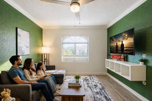 A living room with a sofa, a coffee table, a TV, and a window with blinds.