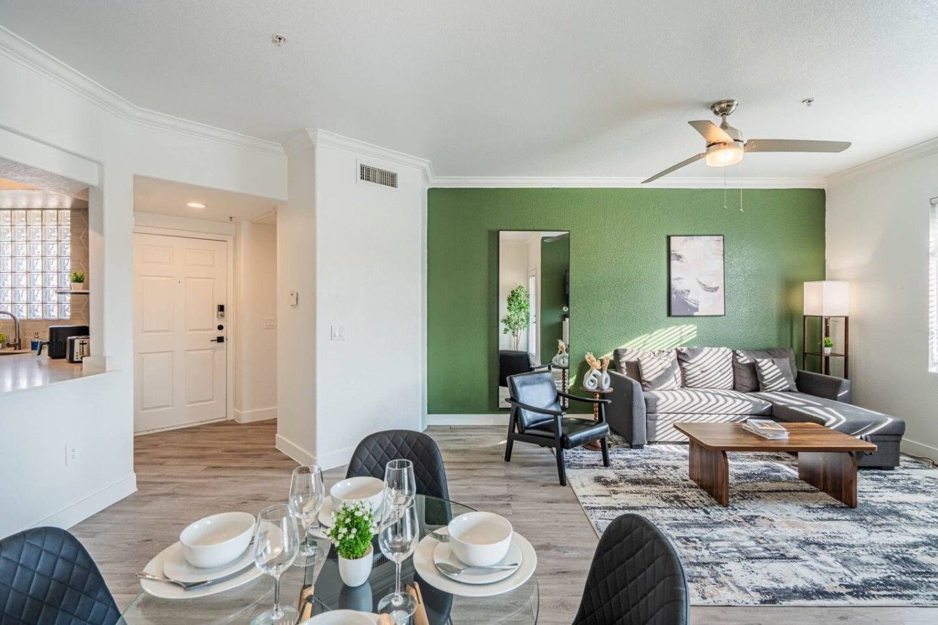 A modern living room with a green accent wall, a dining area with a set table, and a ceiling fan.
