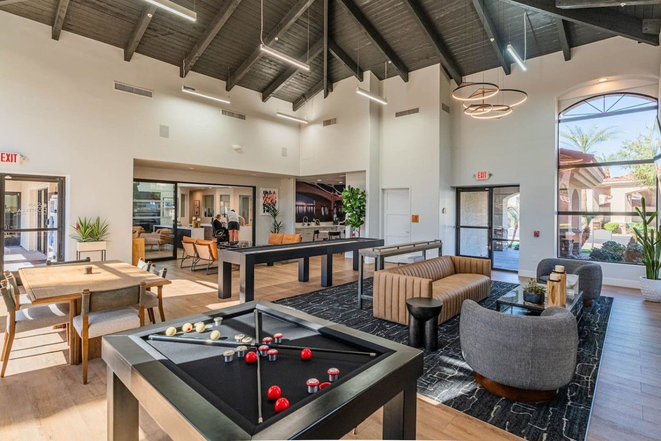 A modern indoor space with a pool table, seating areas, and a kitchen in the background.