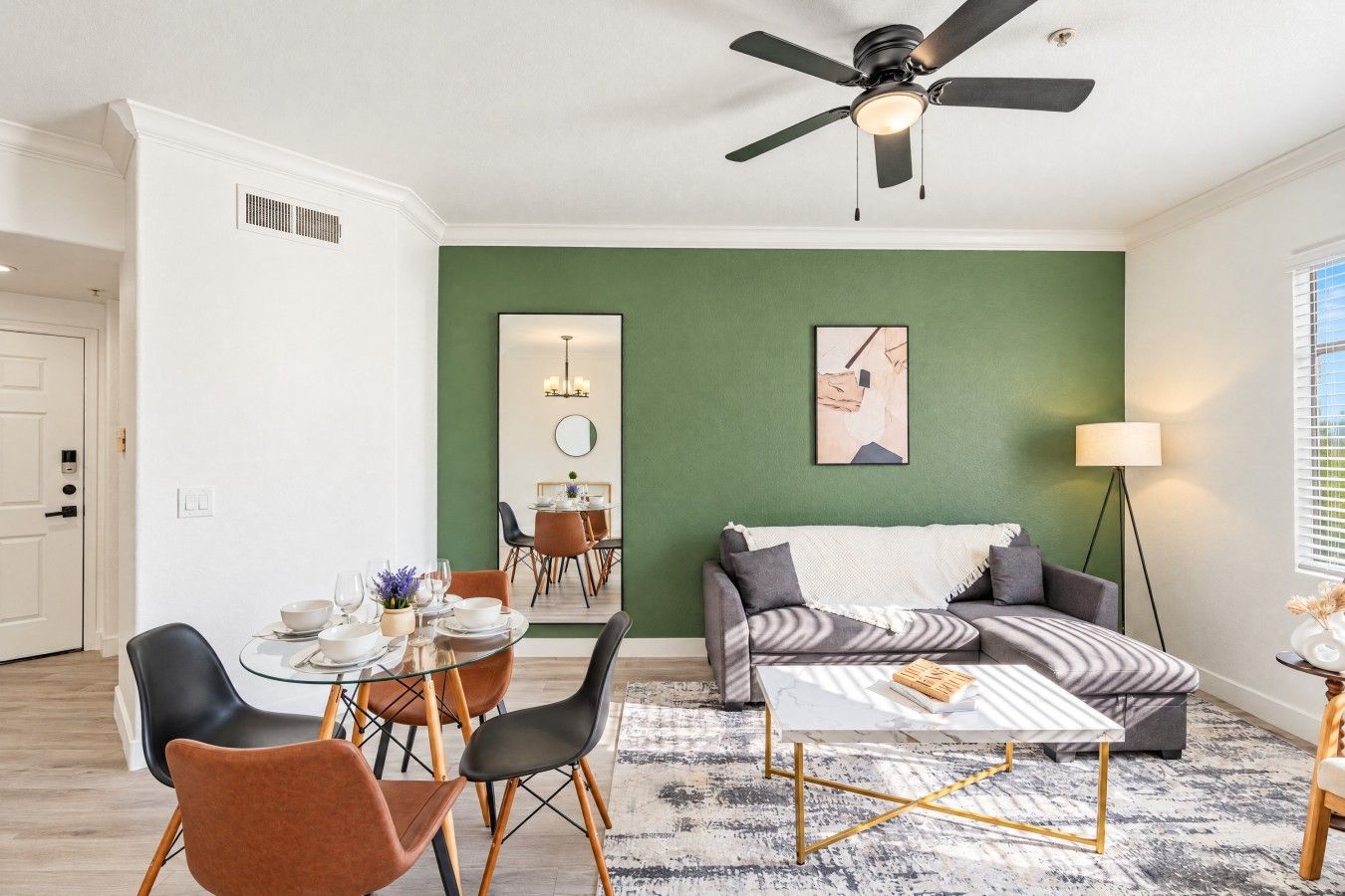 Una sala moderna con comedor, pared de acento verde, ventilador de techo y vista al comedor a través de un espejo.