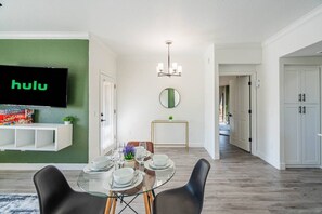 A dining area with a glass table, black chairs, and a wall-mounted TV displaying 'hulu'. - 2BR-2BA Near ASU & Arizona Mills | Pool & W/D (Tempe)