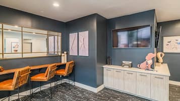 A modern interior with a dark wall, a large mirror, a flat-screen TV, and a wooden desk with chairs.