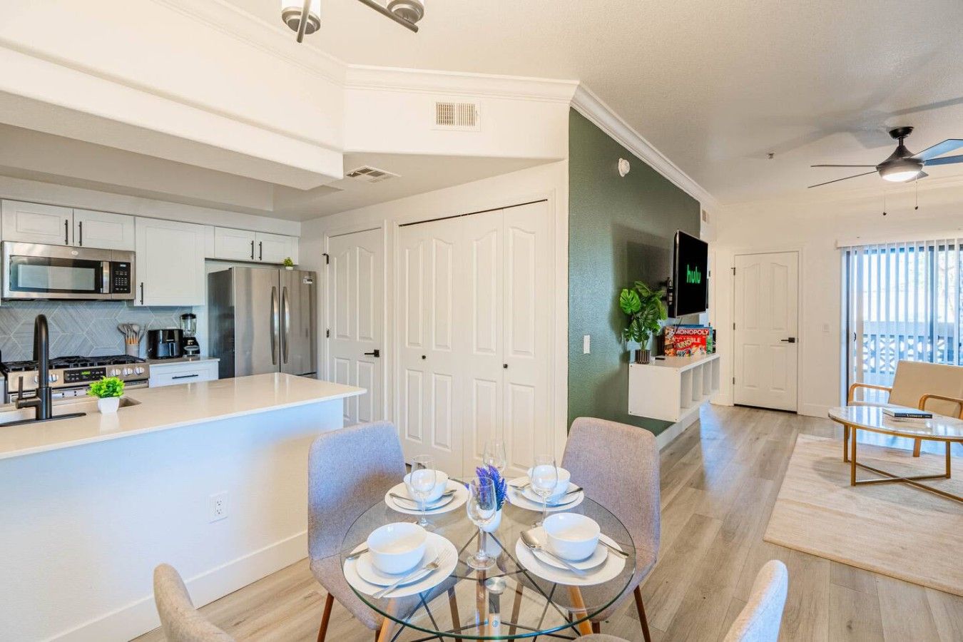 Una cocina moderna con electrodomésticos de acero inoxidable, un comedor con mesa de vidrio y una sala de estar con televisión.