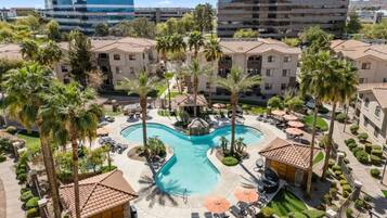 A hotel with a central swimming pool, palm trees, and modern buildings in the background.