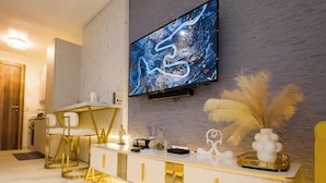 A modern living room with a flat-screen TV mounted on a textured wall, a white console table with gold accents, and a plush area rug. - Cozy studio apt in Accra - Ghana with AC and gym access (Accra)