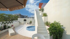 Un espace piscine aménagé sur le toit, avec une piscine circulaire, des murs blancs et une terrasse en bois.