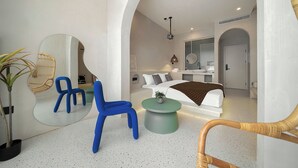 Une chambre d’hôtel moderne avec un grand lit, un coin salon comprenant un fauteuil et une petite table ronde, un grand miroir et une petite plante.