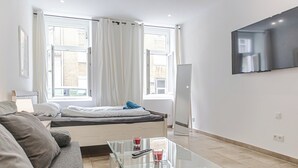 A modern hotel room with a bed, a glass coffee table, a TV mounted on the wall, and a window with curtains. - Central Vienna Elegant 1BR Apartment (Vienna)