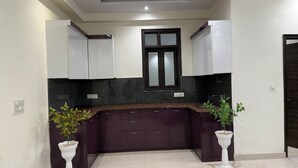 Une cuisine moderne avec des meubles de couleur violet foncé, un plan de travail noir et une fenêtre au-dessus de l’évier.