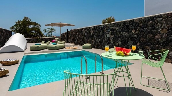 A swimming pool with lounge chairs and a table with drinks and fruit. - MODERN DOME HOMES OF SANTORINI (Santorini)