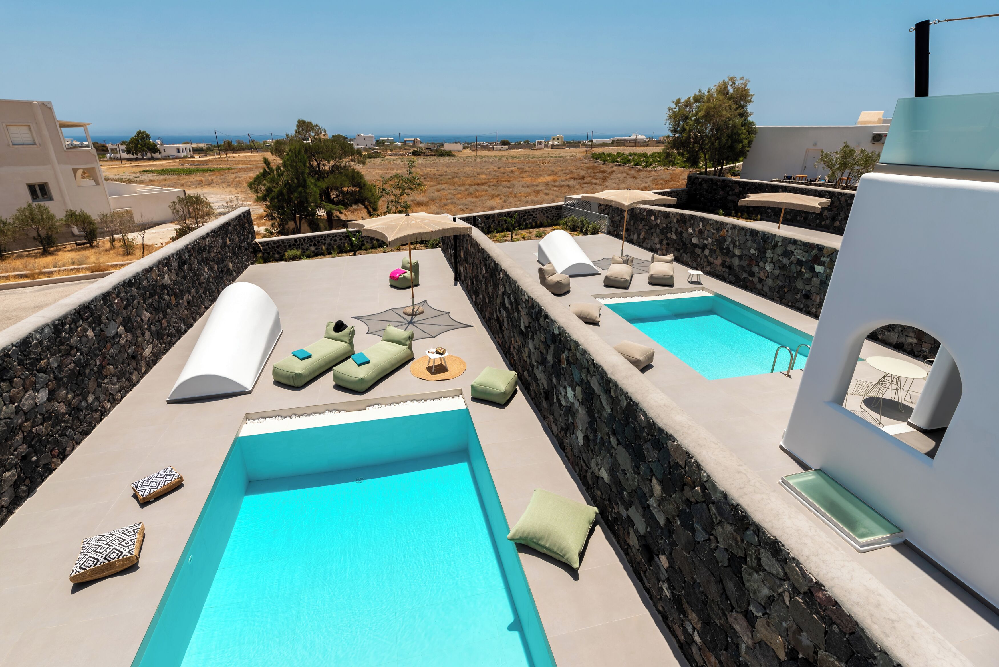 A rooftop pool area with two pools, lounge chairs, and a stone wall.