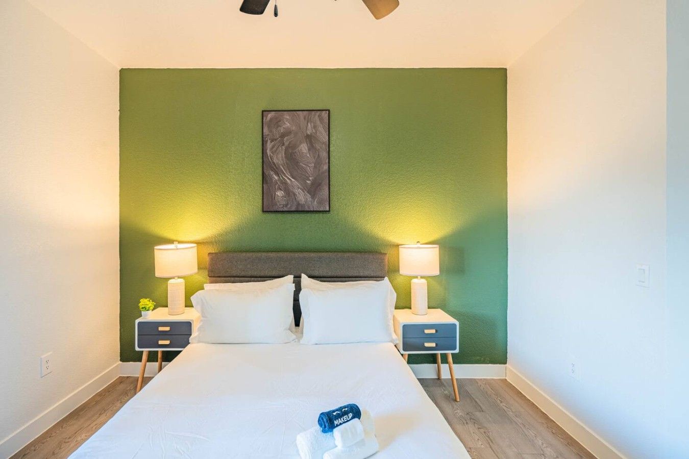 Ein Hotelzimmer mit einem Bett, zwei Nachttischen, zwei Lampen, einem Wandbild und einem Deckenventilator.
