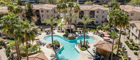 A hotel with a central swimming pool, palm trees, and a modern building in the background.
