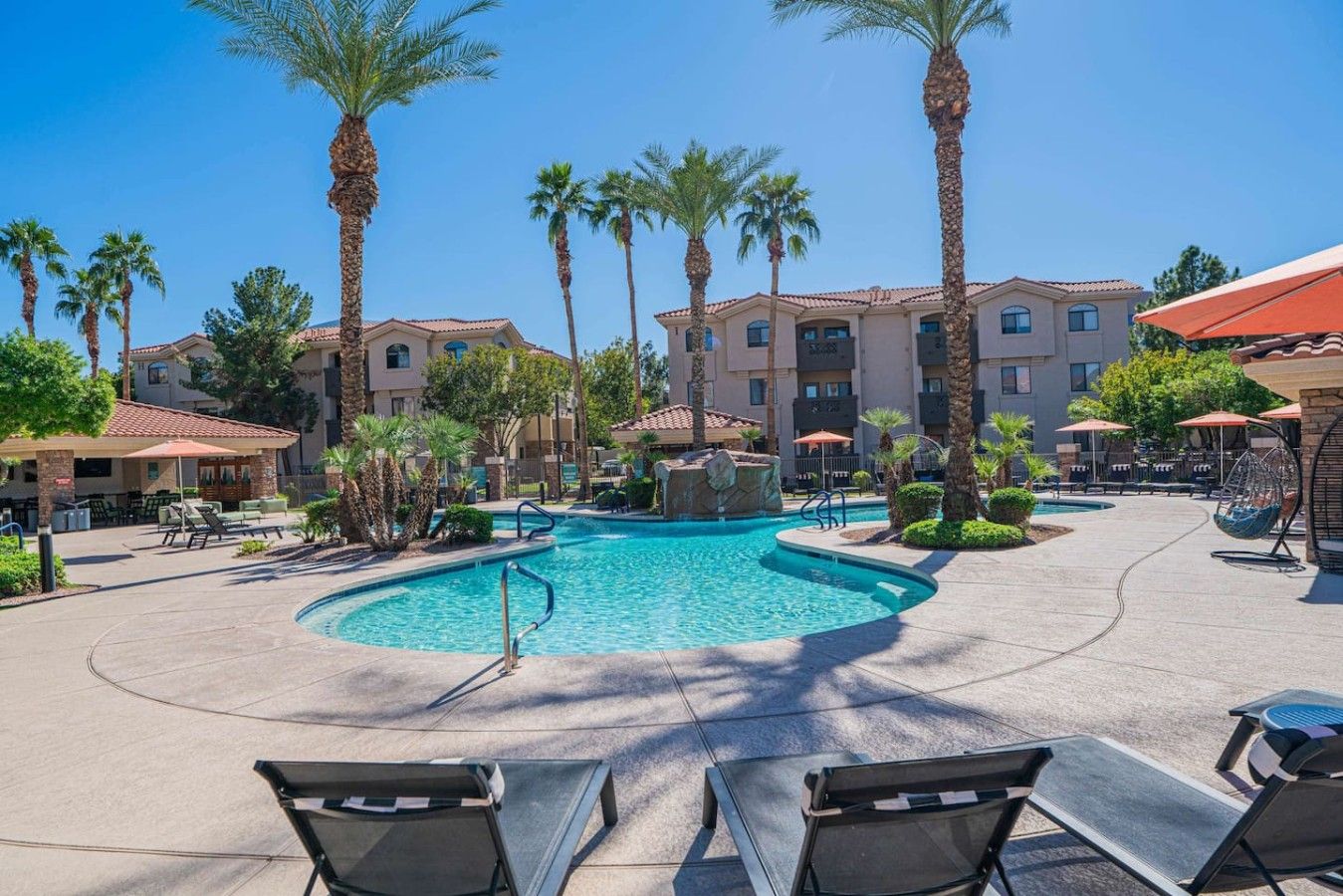 A resort pool area with lounge chairs, palm trees, and a building with multiple balconies.