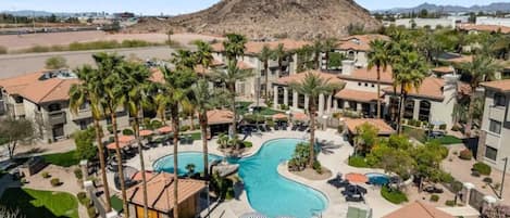 A resort with a swimming pool, palm trees, and a mountain in the background.