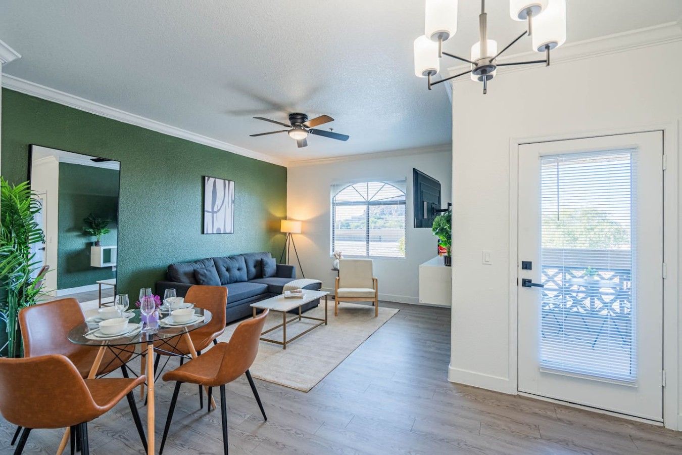 A modern living room with a dining area, a ceiling fan, and a large window with blinds.