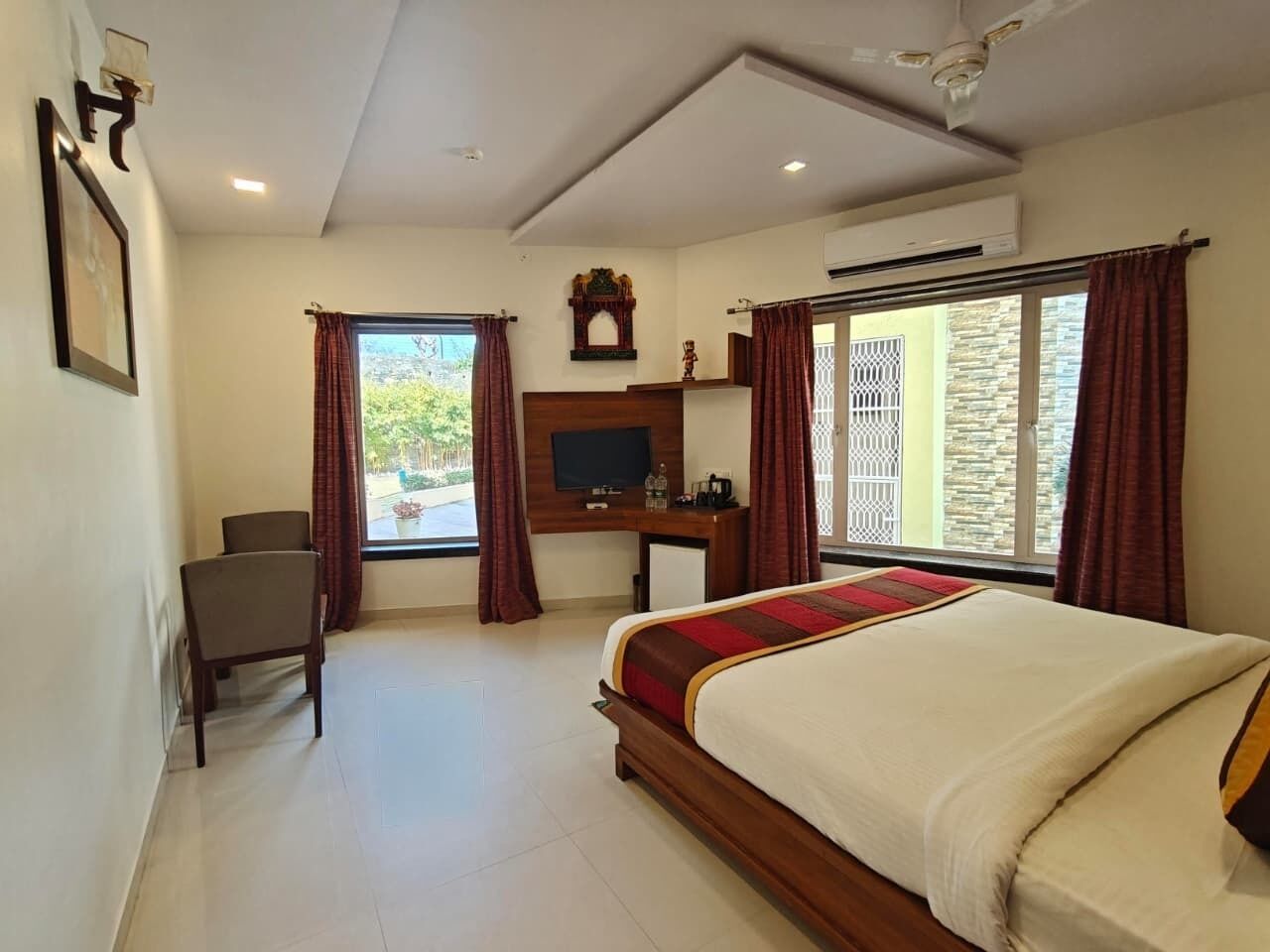 A hotel room with a bed, a desk, a chair, a TV, and a window with curtains.
