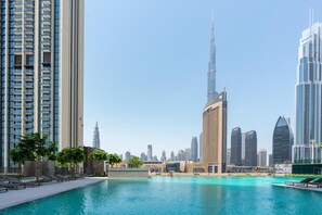 A modern urban landscape with a prominent skyscraper, a marina with boats, and a pool area. - Downtown Views II - Tower 2 (Dubai)