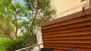En balkon med to fletstole og et lille bord, gelænder i metal, samt udsigt til grønt og en bygning.