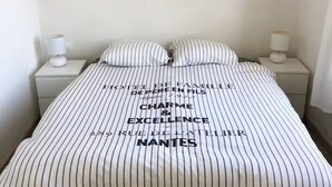Un lit d’hôtel avec une literie et des oreillers à rayures, une table de chevet avec une lampe et une lampe fixée au mur.