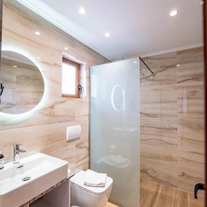 Ein modernes Badezimmer mit großem Spiegel, Waschbecken, Toilette und einer Duschkabine aus Glas.
