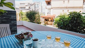 Un tavolo con tovaglia a quadri, un vassoio con tazze e bicchieri, e vista su edifici e vegetazione.