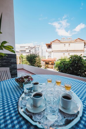 A table with a checkered tablecloth, a tray with cups and glasses, and a view of buildings and greenery. - Marilena's Garden (Ksamil)