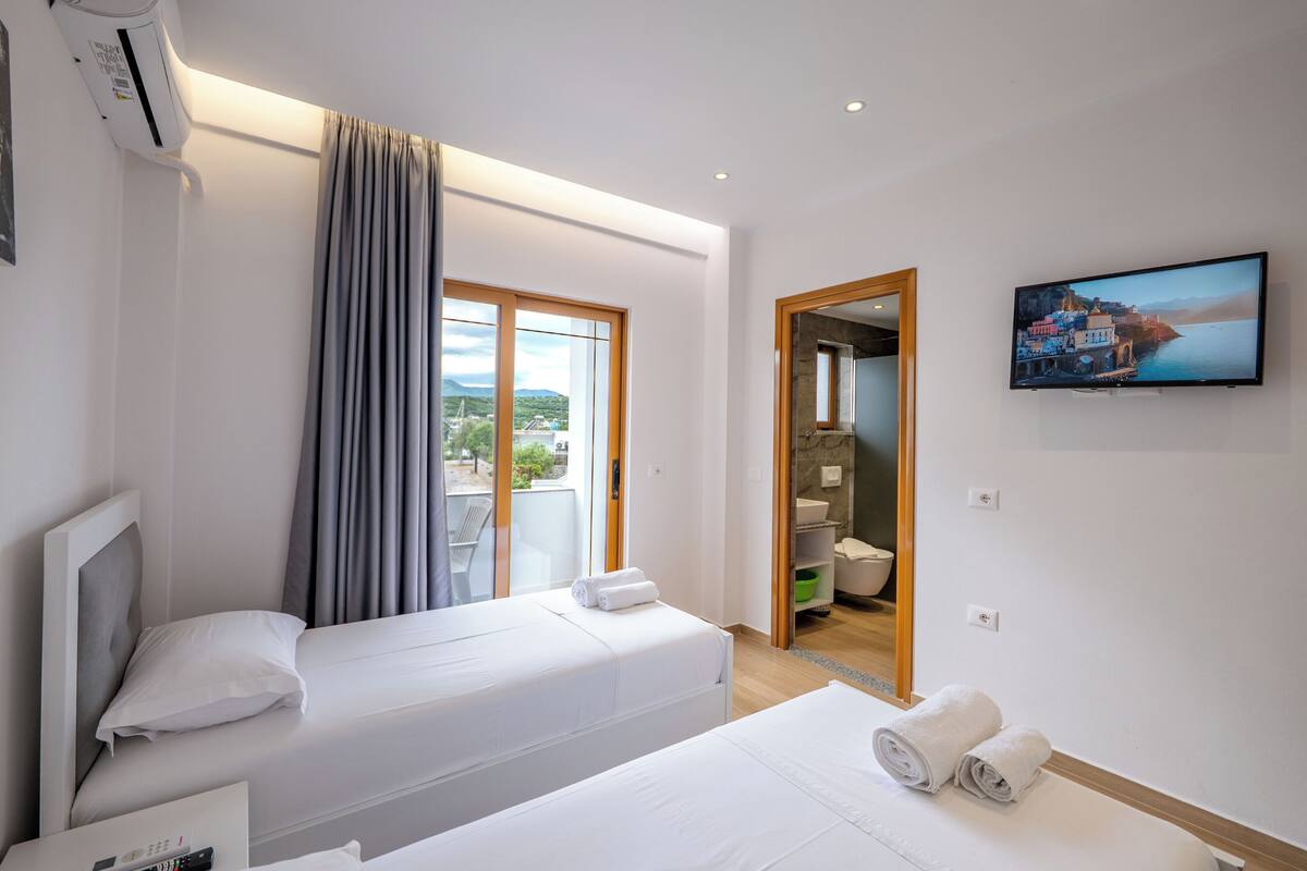 Una camera d'albergo con due letti, una TV e un bagno visibile attraverso una porta aperta.