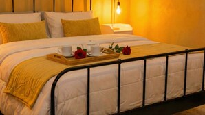A neatly made bed with a tray of white cups and a red rose, a bedside table with a lamp, and a warm wall color. - Navona Apartment (Rome)